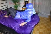 Pia tied, gagged and hooded with cuffs and chains on a bed wearing a sexy black rain pants and a blue down jacket (Pics)