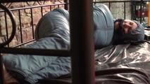 Mara tied, gagged and hooded on bed in a cellar wearing a shiny blue/grey downwear (Video)