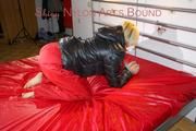 Sonja tied and gagged with a pillory on bed wearing a sexy red rain pants and a black down jacket (Pics)