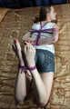 Barefoot Elly in tank-top and jeans shorts, hogtied with hemp rope, poses for the camera