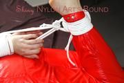 Mara tied and gagged on bed wearing a sexy shiny nylon catsuit in red (Pics)