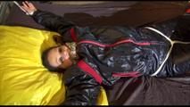 Liz tied and gagged on a bed wearing an oldschool black/red shiny nylon downwear combination (Video)