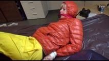 Pia tied and gagged on bed wearing a yellow rain pants and an orange downjacket (Video)
