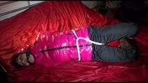 Mara tied, gagged and hooded on a bed wearing a supersexy black rain pants and a pink down jacket (Video)