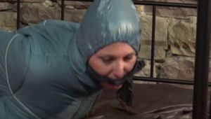 Mara tied, gagged and hooded on bed in a cellar wearing a shiny blue/grey downwear (Video)