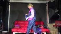 Watching Pia wearing a blue/purple/pink shiny nylon rain suit folding clothes and tidying up the studio (Video)
