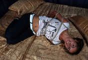 Barefoot Christy in white t-shirt and black jeans, hogtied with hemp rope, wiggles on the bed