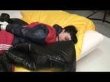 Jill tied and gagged on bed wearing a red shiny nylon shorts and a blue/red rainjacket (Video)