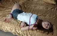 Barefoot Elly in tank-top and jeans shorts, hogtied with hemp rope, poses for the camera