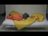 Samantha tied and gagged in bed wearing an orange/grey shiny nylon rainwear combination (Video)