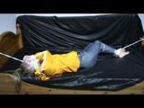 Samantha in a shiny yellow rain jacket and a shiny grey rain trowsers tied and gagged on bed (Video)