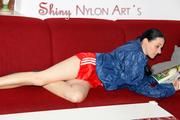 Lucy wearing a sexy red shiny nylon shorts and a blue shiny nylon rain jacket during reading a bit on the sofa (Pics)