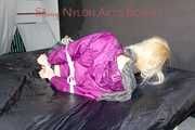 Pia tied and gagged on a bed with belts wearing a sexy black shiny nylon shorts and a purple shiny nylon rain jacket (Pics)