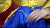 Sonja wearing a blue rain pants and a yellow PAMY down jacket while bonding herself an the sofa (Video)