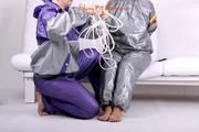 Sophie tied and gagged by Jill on a sofa wearing a shiny silver PVC sauna suit which is slitted by Jill (Pics)