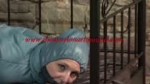 Mara tied, gagged and hooded on bed in a cellar wearing a shiny blue/grey downwear (Video)