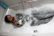 Simone in an shiny grey pvc sauna suit tied and gagged by Sophie in the bath tub (pics)