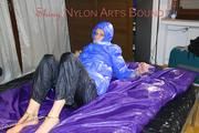 Pia tied, gagged and hooded with cuffs and chains on a bed wearing a sexy black rain pants and a blue down jacket (Pics)