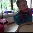 Mara tied and gagged on a chair with a bar at her back wearing a blue shiny nylon rain pants and a green rain jacket (Video)