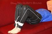 Mara tied and gagged on a sofa wearing a shiny black rain pants and a sexy lightblue down jacket (Video) 