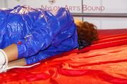 Lulu tied and gagged on a bed wearing a blue shiny nylon shorts and a blue rainjacket (Pics)