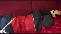 Lucy tied and gagged with ropes and a cloth gag on a sofa wearing a blue/red rainwear combination (Video)