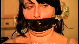 22 YEAR OLD FEISTY DEREK IS MUMMY WRAPPED WITH CLEAR PLASTIC, ELECTRICAL TAPE BOUND & WRAP GAGGED, MOUTH STUFFED & BLACK LEATHER GLOVE HANDGAGGED (D66-10)