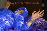 Pia tied, gagged and hooded with cuffs and chains on a bed wearing a sexy black rain pants and a blue down jacket (Pics)
